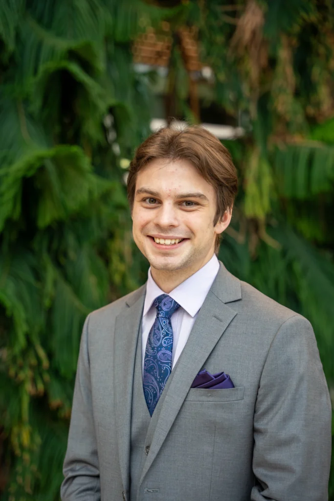 Cameron Prosic, candidate for HWDSB public school trustee in Ward 1, smiling in a grey suit and purple paisley tie