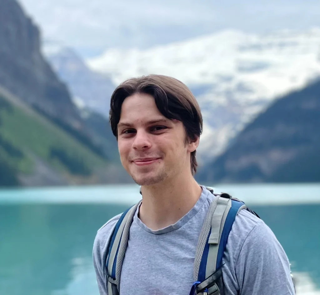 Cameron Prosic smiling outdoors at Lake Louise, with mountains behind him